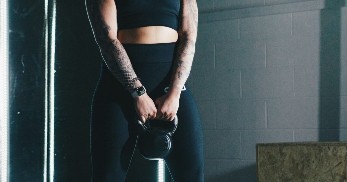 a woman with tattoos holding a kettle in a gym