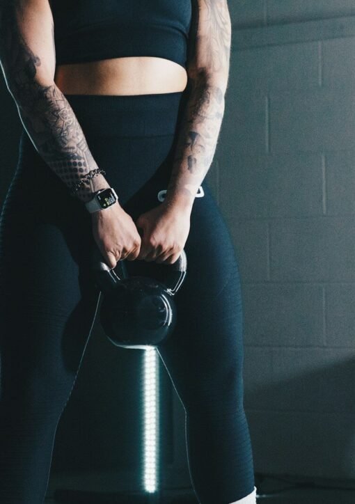 a woman with tattoos holding a kettle in a gym