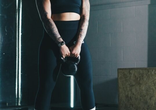 a woman with tattoos holding a kettle in a gym
