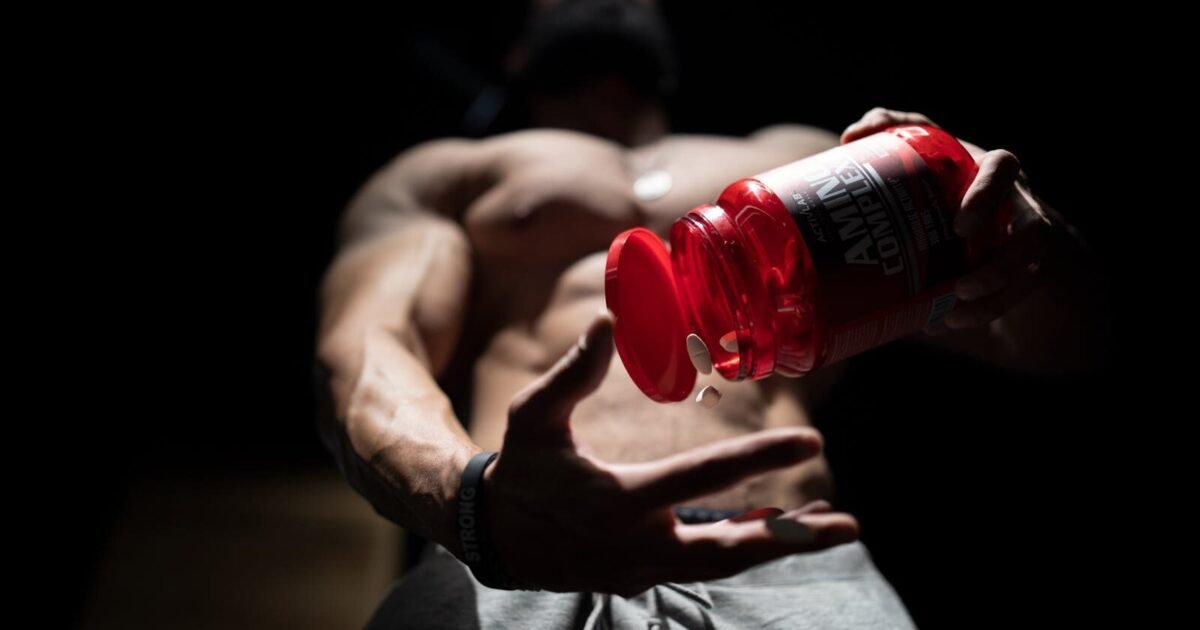 Shirtless muscular man pouring protein supplements from a bottle, showcasing fitness and strength.