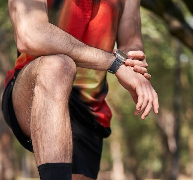 Close-up of an athlete resting on a park bench, emphasizing fitness gear and smartwatch.