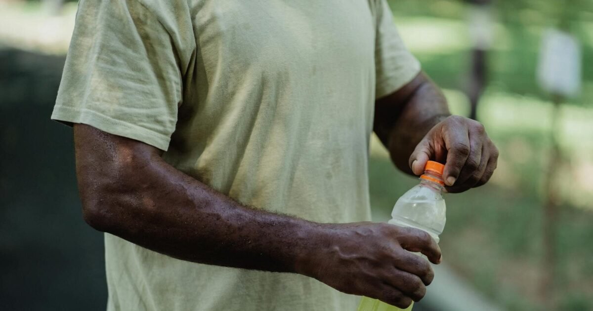 Close-up of a person opening a bottle of sports drink in a park setting.