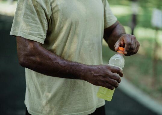 Close-up of a person opening a bottle of sports drink in a park setting.