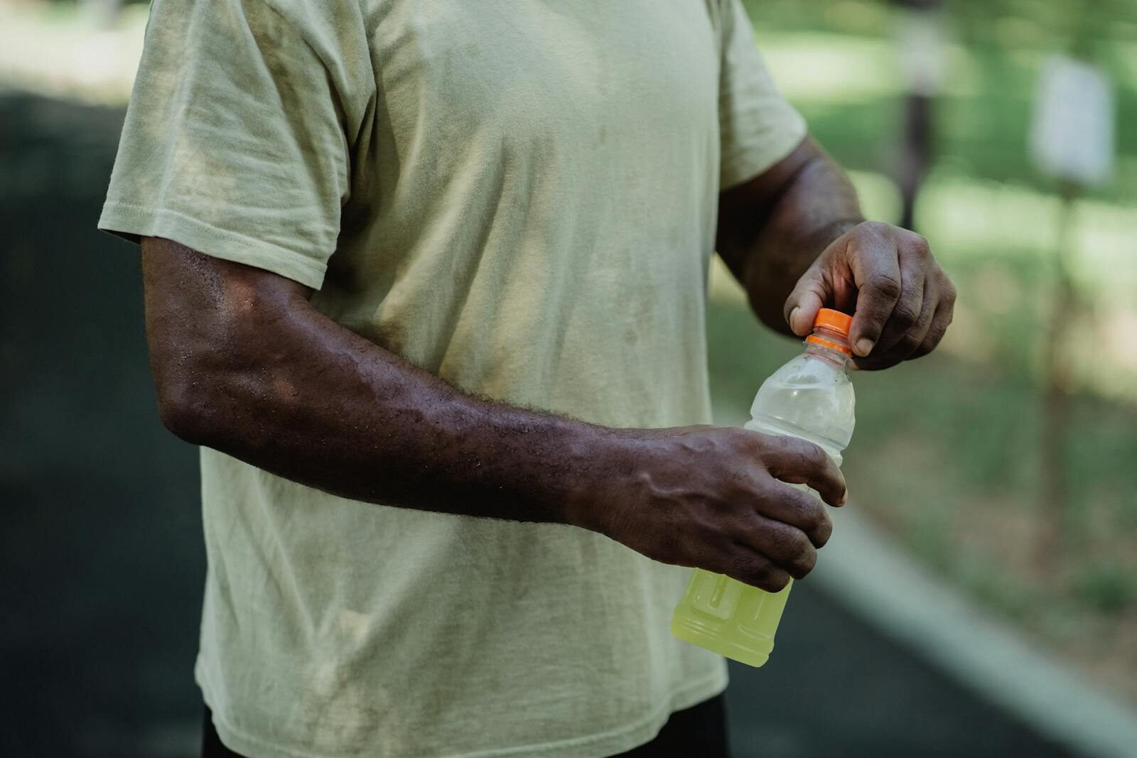 Close-up of a person opening a bottle of sports drink in a park setting.