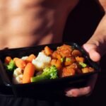 person holding black plastic container with food