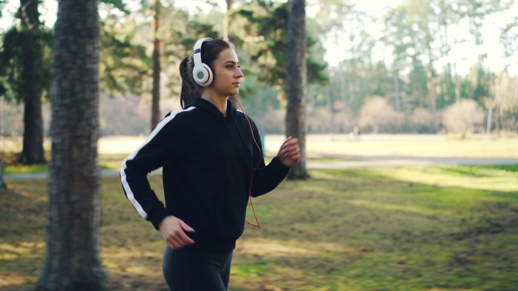 Benefícios de correr com música: corredora em parque usando fones.
