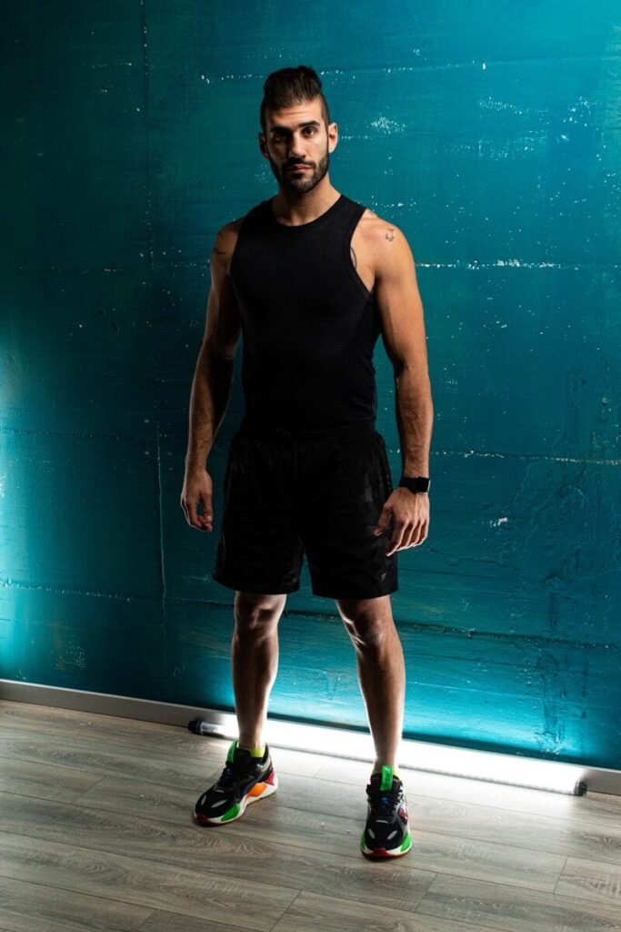 Homem usando regata e bermuda de treino preta em frente a uma parede azul, exemplificando vestuário de treino confortável.