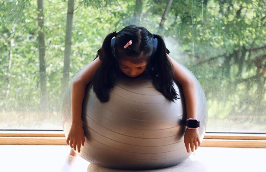 Mulher sentada em uma Fitball em frente à janela praticando consciência corporal.