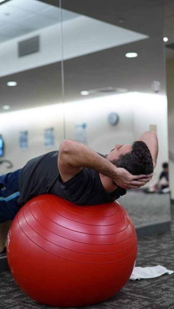 Homem realizando exercício de core deitado sobre uma Fitball vermelha.